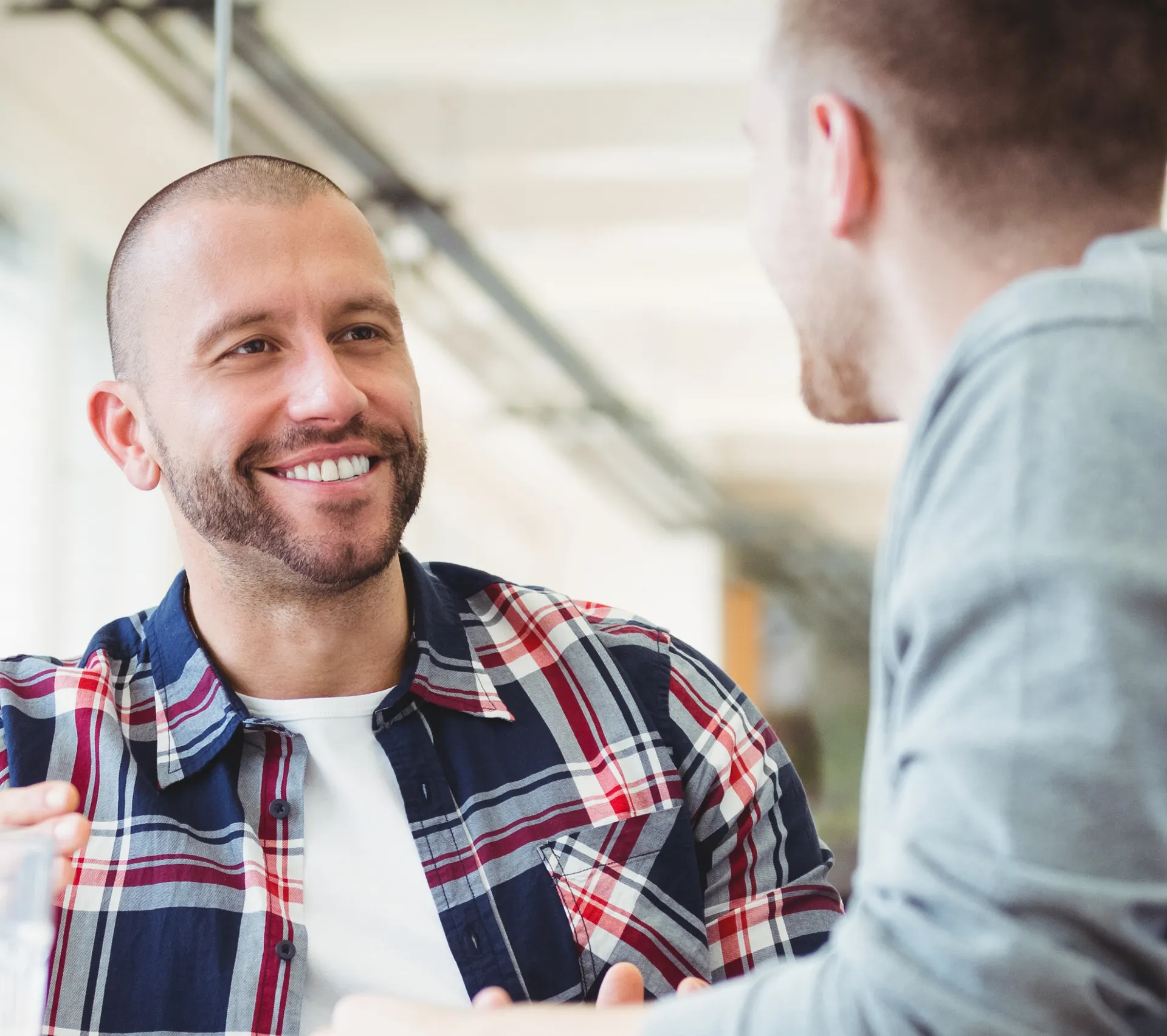 A smiling man in a checked shirt chatting with an adviser during a supportive one-to-one conversation.