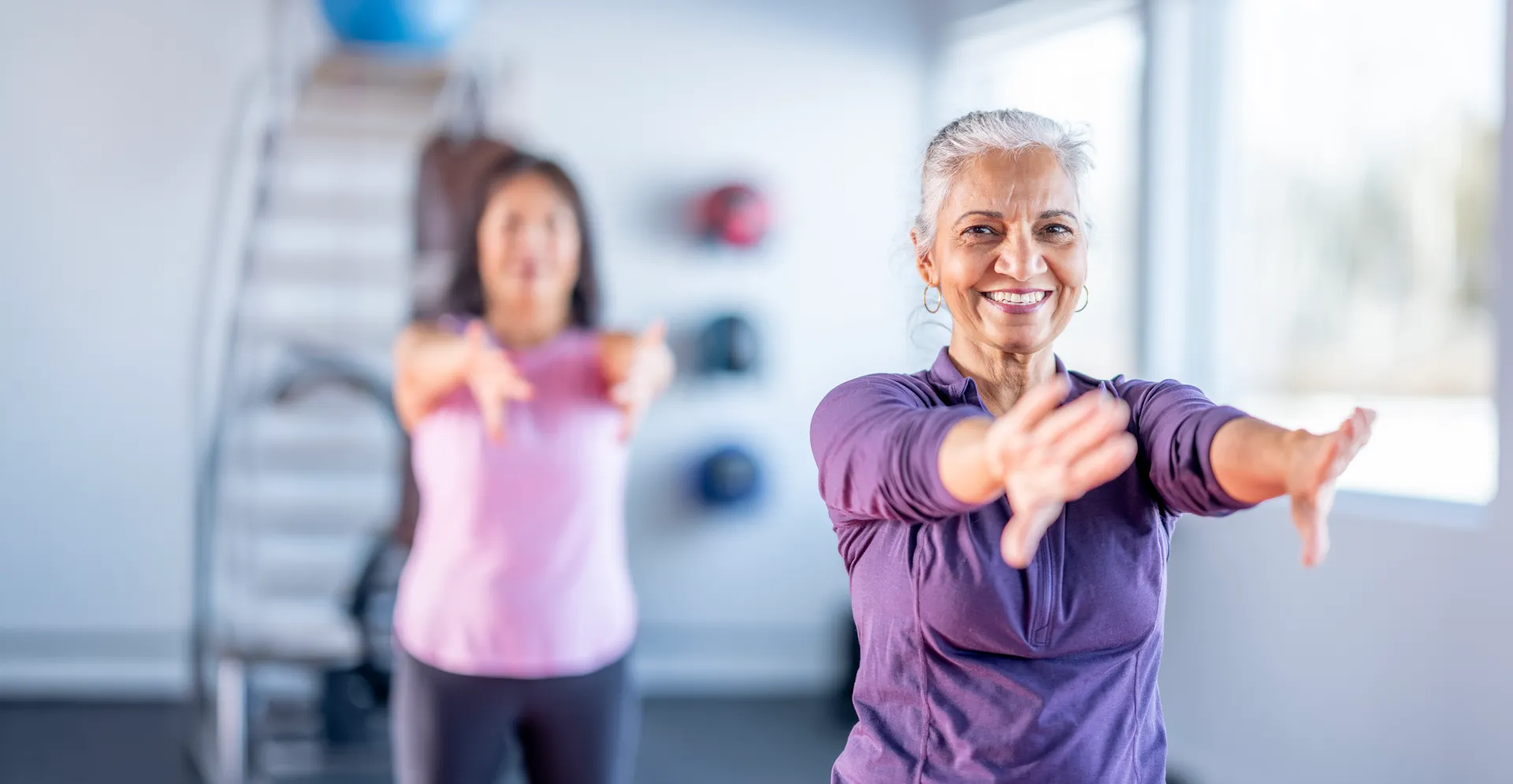 Two women practising tai chi together in a bright exercise studio.
